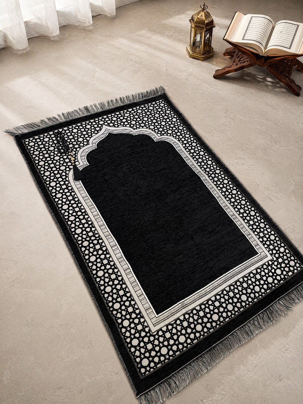 Black Ayahly prayer mat with woven arch design laid out beside a lantern and Quran stand