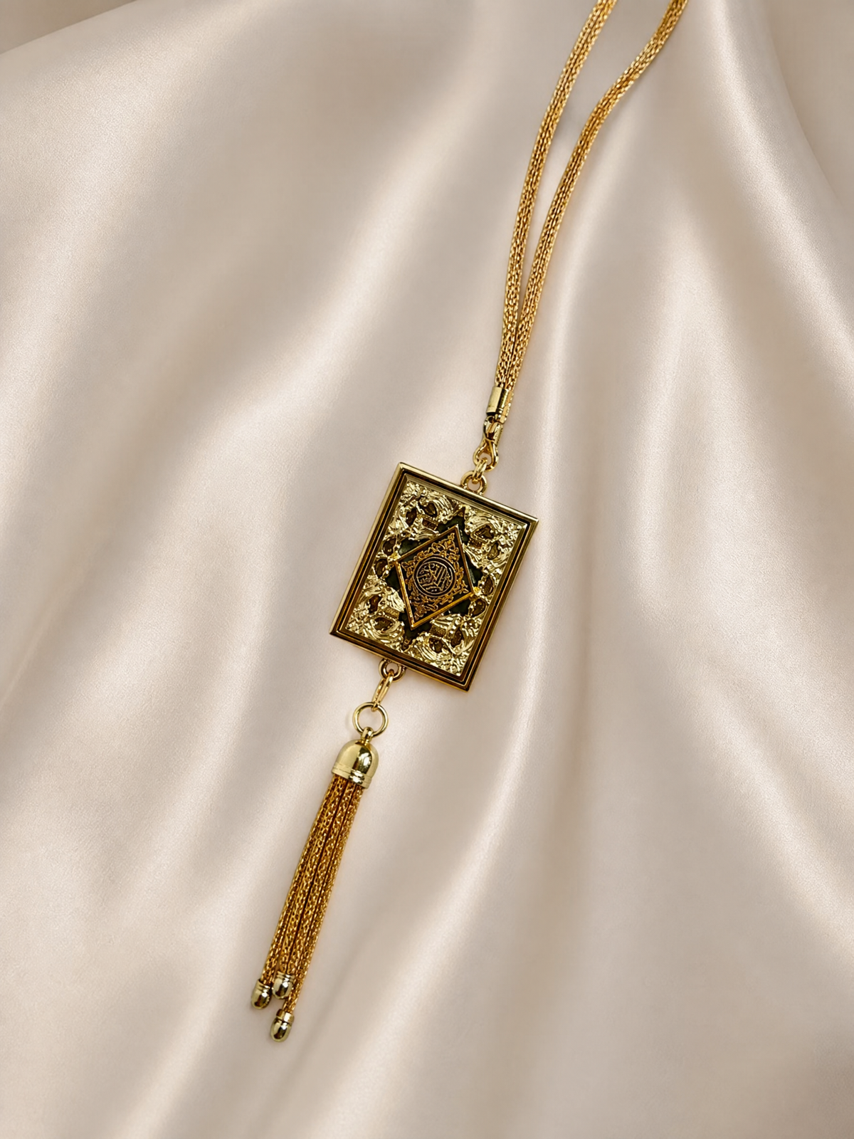 Gold mini Quran book pendant with tassel resting on cream silk