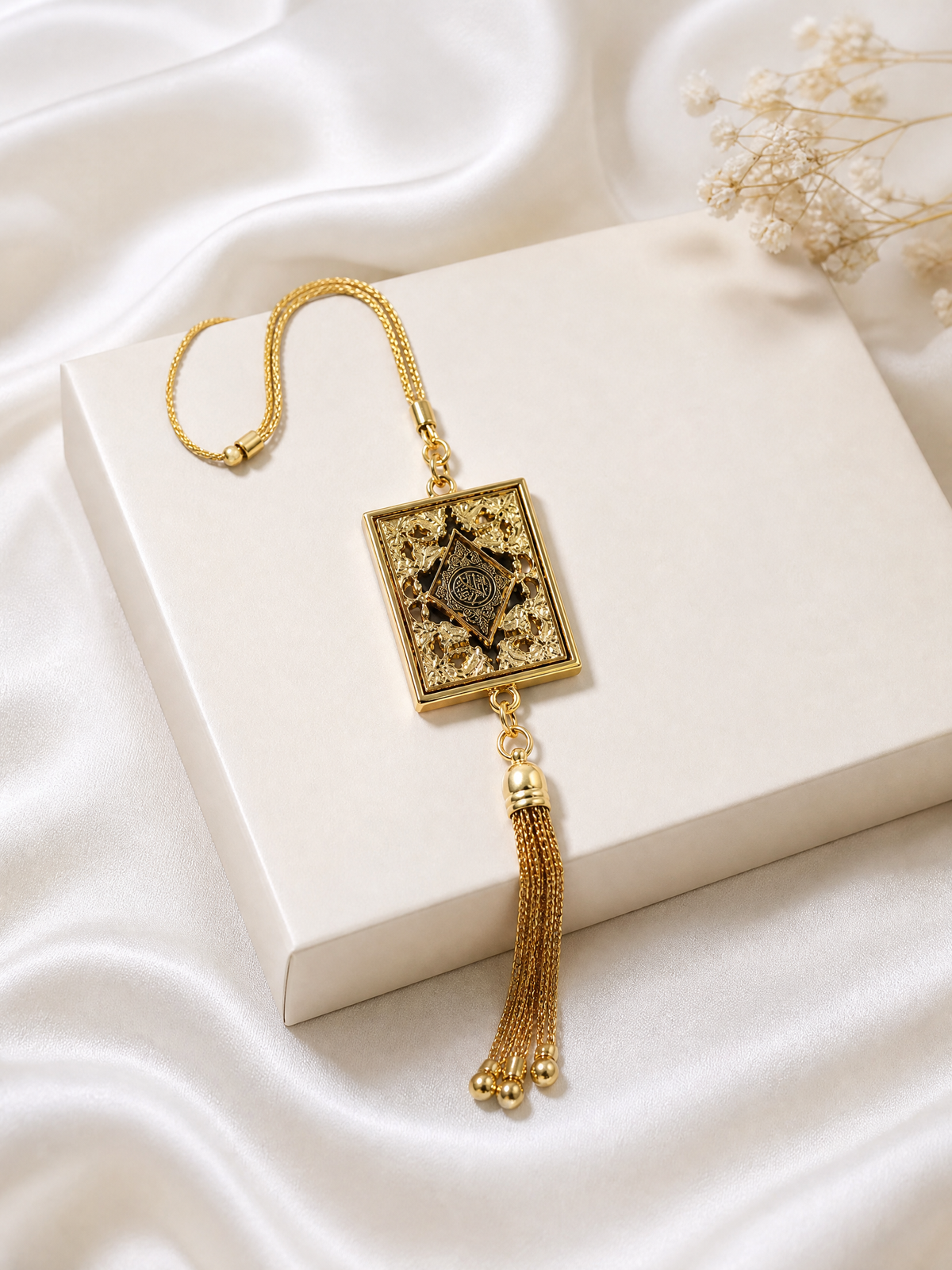 Close-up of the gold mini Quran ornament showing its engraved cover and fine chain