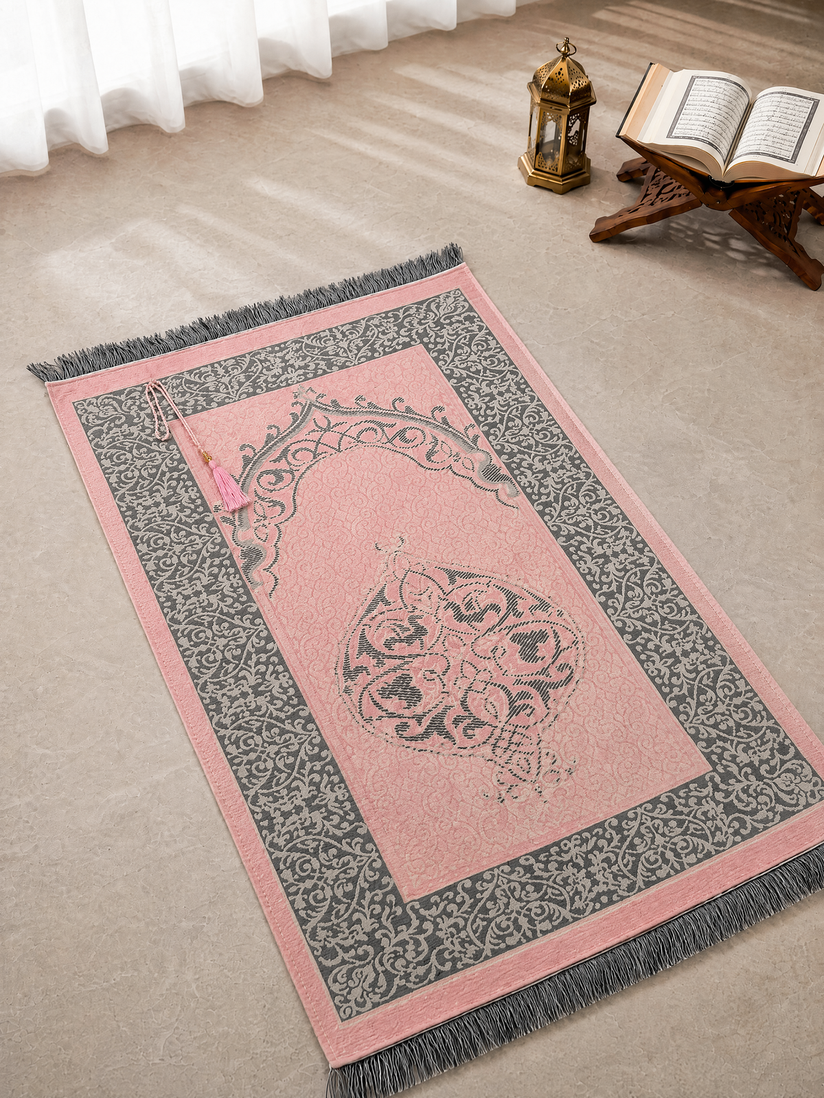 Pink Ayahly prayer mat with woven arch design laid out beside a lantern and Quran stand