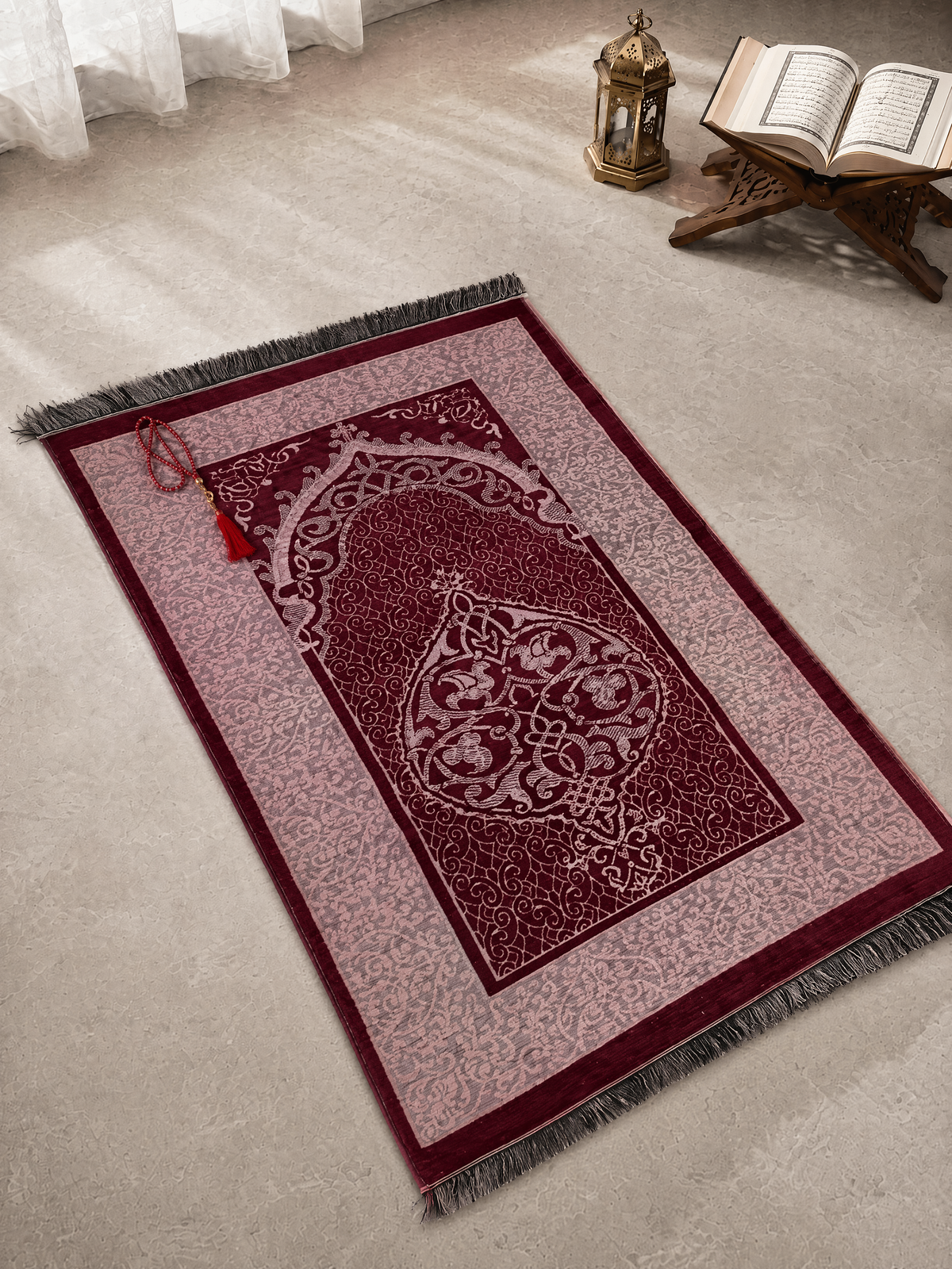 Maroon red Ayahly prayer mat with woven arch design laid out beside a lantern and Quran stand