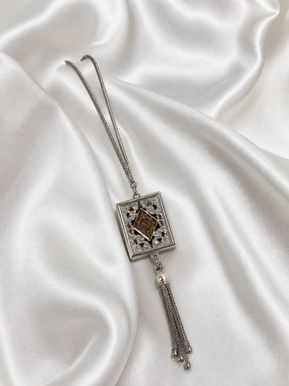 Silver mini Quran book pendant with tassel resting on white silk